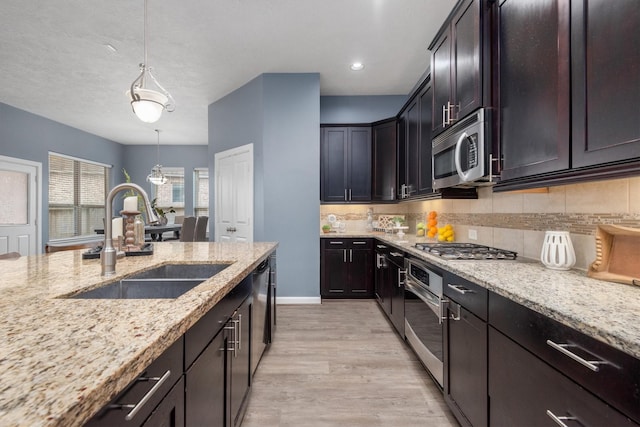 kitchen with tasteful backsplash, light wood finished floors, light stone countertops, appliances with stainless steel finishes, and a sink