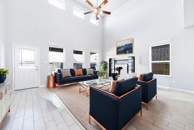 living room featuring light wood-style flooring, baseboards, ceiling fan, and a fireplace