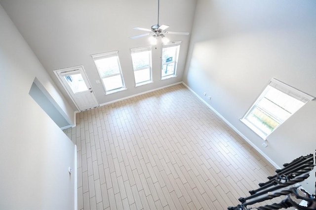 unfurnished living room with baseboards, high vaulted ceiling, and a ceiling fan