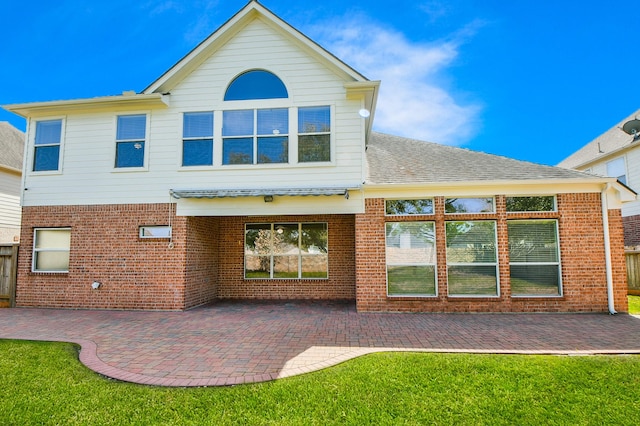 rear view of house featuring a patio area, a lawn, a shingled roof, and brick siding