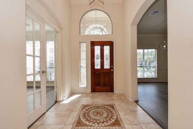 tiled entryway featuring visible vents, arched walkways, baseboards, and crown molding