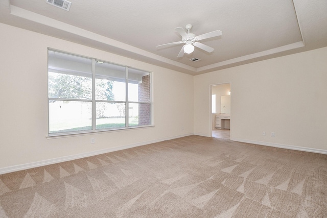 empty room featuring a tray ceiling, light colored carpet, and visible vents