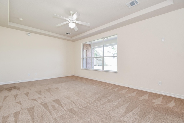 empty room with baseboards, visible vents, ceiling fan, light carpet, and a raised ceiling