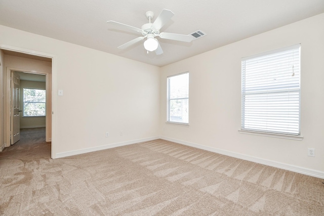 spare room with a wealth of natural light, baseboards, light colored carpet, and ceiling fan