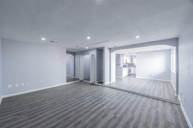 unfurnished living room with visible vents, baseboards, wood finished floors, arched walkways, and a textured ceiling