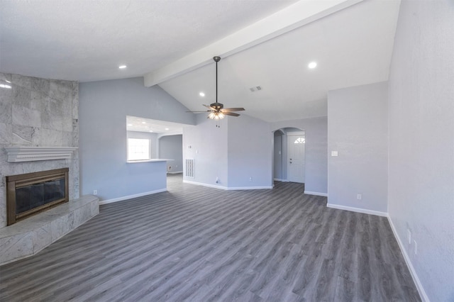 unfurnished living room featuring a ceiling fan, a tiled fireplace, lofted ceiling with beams, wood finished floors, and arched walkways