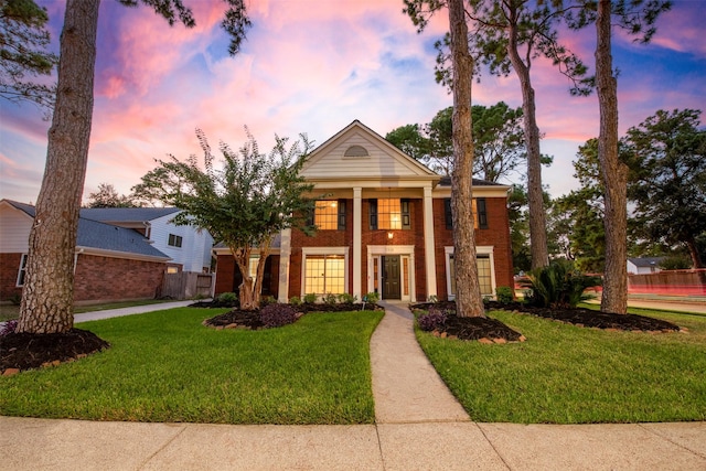 greek revival house with a garage, brick siding, a front yard, and fence