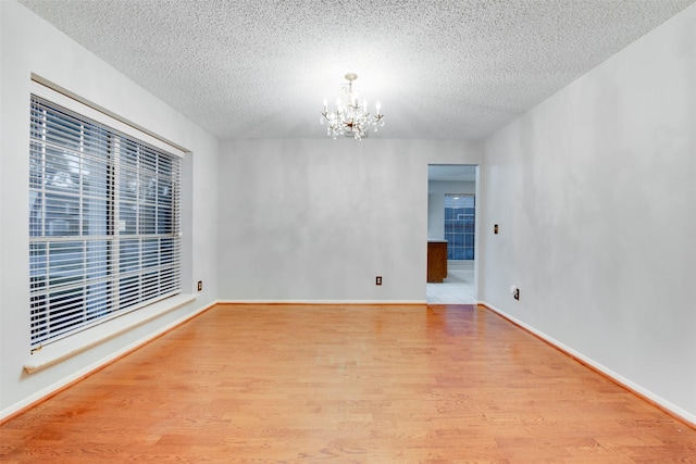 unfurnished room featuring baseboards, wood finished floors, a textured ceiling, and a chandelier