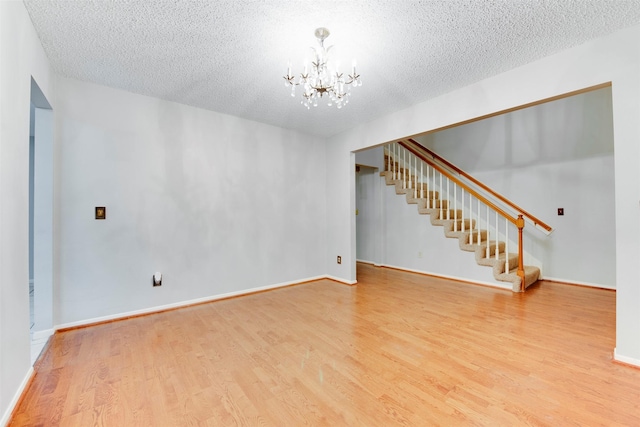 unfurnished living room with baseboards, stairway, an inviting chandelier, wood finished floors, and a textured ceiling