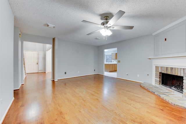 unfurnished living room with wood finished floors, a ceiling fan, visible vents, a fireplace, and a textured ceiling