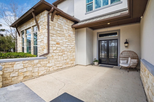 doorway to property with stone siding, stucco siding, french doors, and a standing seam roof