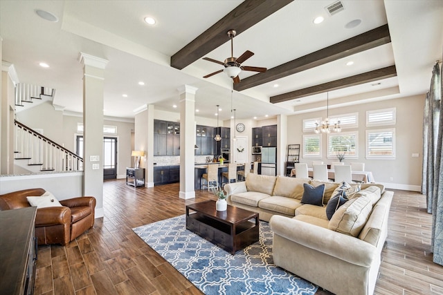 living room with visible vents, ceiling fan with notable chandelier, wood finished floors, stairs, and ornate columns