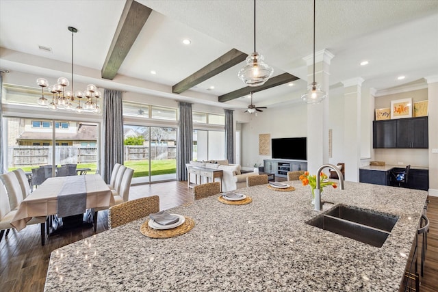 kitchen featuring dark wood finished floors, beamed ceiling, an island with sink, ceiling fan with notable chandelier, and a sink