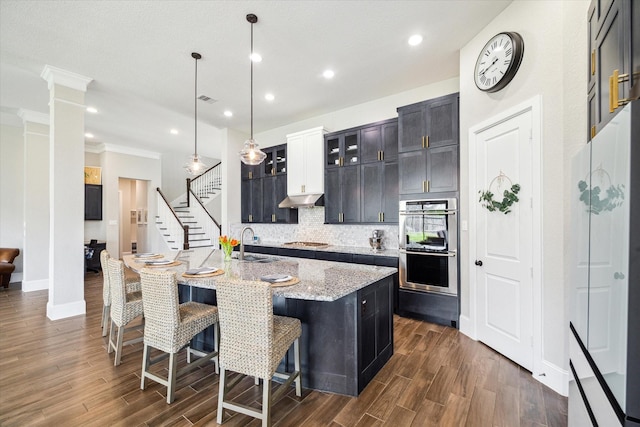 kitchen with a sink, a kitchen breakfast bar, tasteful backsplash, dark wood finished floors, and appliances with stainless steel finishes