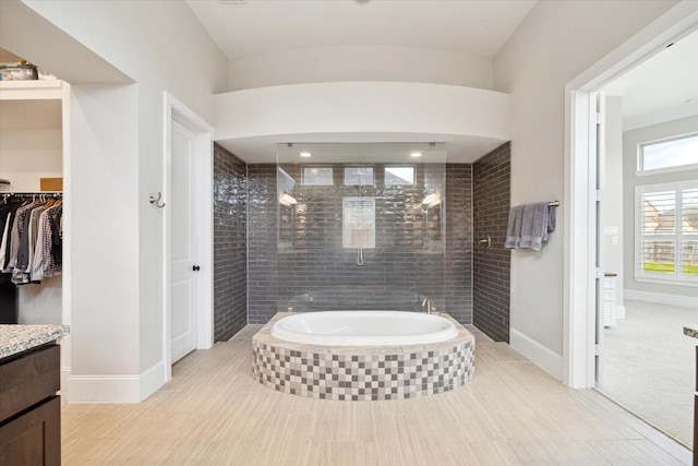 full bathroom featuring a walk in closet, a garden tub, baseboards, tiled shower, and vanity