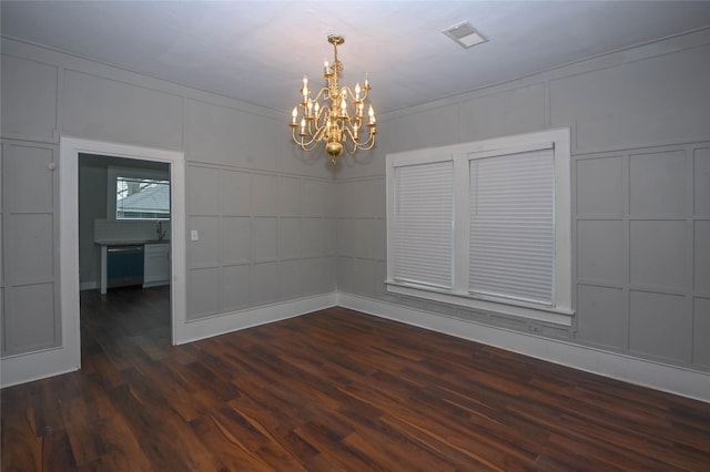 spare room featuring visible vents, a decorative wall, dark wood-style floors, a notable chandelier, and a sink