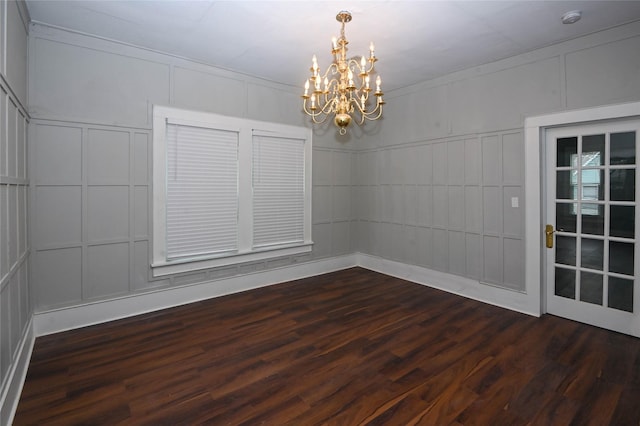 spare room with an inviting chandelier, dark wood finished floors, and a decorative wall