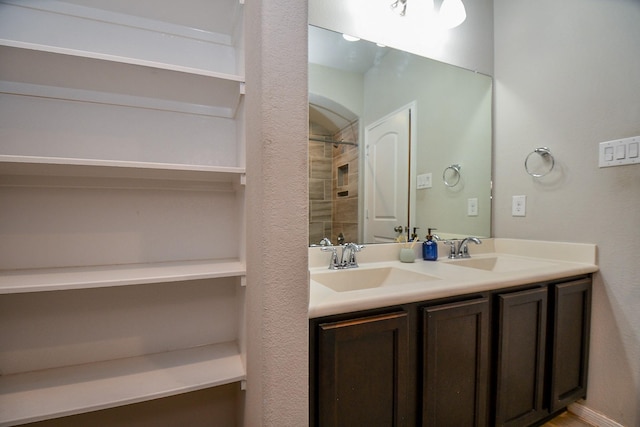 full bath featuring double vanity, a tile shower, and a sink