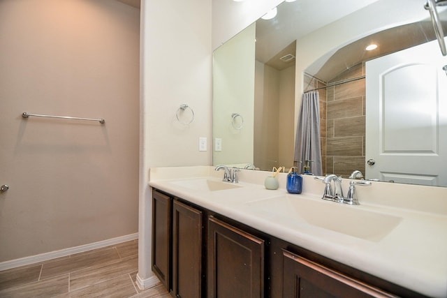 full bath featuring double vanity, wood finish floors, baseboards, and a sink