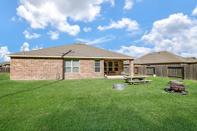 back of house featuring brick siding, an outdoor fire pit, a yard, and fence