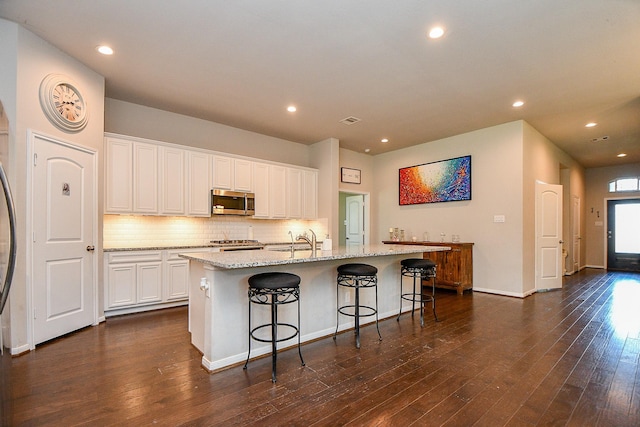 30903 Roanoak Woods Dr, Tomball, TX 77375 - kitchen with stainless steel microwave, a sink, a kitchen island with sink, light stone counters, and decorative backsplash