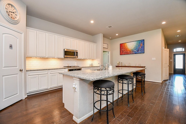 kitchen with visible vents, dark wood-style flooring, a sink, stainless steel microwave, and backsplash