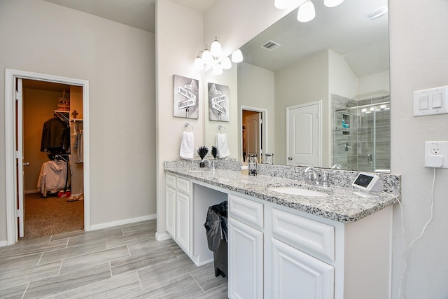 bathroom featuring a shower stall, a walk in closet, baseboards, double vanity, and a sink