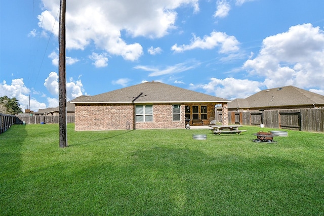 back of house featuring an outdoor fire pit, a yard, a fenced backyard, a shingled roof, and brick siding