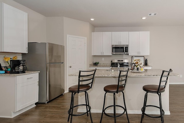 kitchen featuring visible vents, a kitchen bar, stainless steel appliances, dark wood-style floors, and white cabinetry