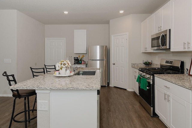 kitchen featuring a breakfast bar area, dark wood-style floors, an island with sink, a sink, and appliances with stainless steel finishes