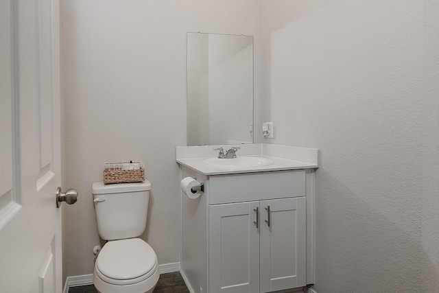 half bath featuring toilet, vanity, and baseboards