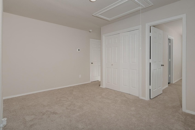 unfurnished bedroom featuring a closet, baseboards, attic access, and carpet flooring