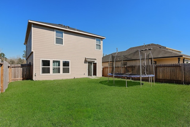 rear view of house featuring a trampoline, a fenced backyard, and a lawn