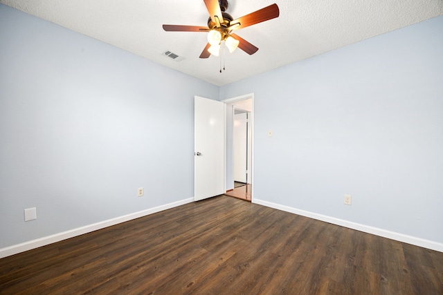 empty room featuring dark wood-style floors, a ceiling fan, visible vents, and baseboards