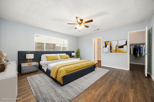 bedroom with a spacious closet, visible vents, wood finished floors, a closet, and a ceiling fan