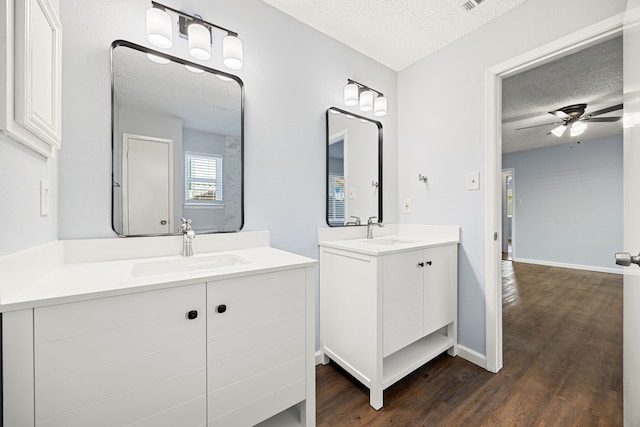 bathroom featuring a sink, a textured ceiling, two vanities, and wood finished floors