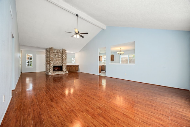 unfurnished living room featuring wood finished floors, a fireplace, beamed ceiling, ceiling fan with notable chandelier, and a wealth of natural light