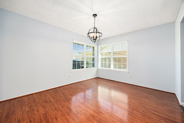 spare room featuring a notable chandelier, wood finished floors, baseboards, and a textured ceiling