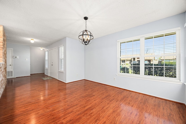 empty room with a textured ceiling, wood finished floors, visible vents, and a chandelier