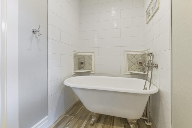 bathroom with tile walls, a freestanding tub, and wood finish floors