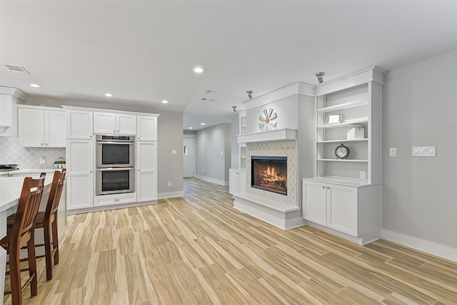 unfurnished living room featuring recessed lighting, visible vents, a glass covered fireplace, and light wood finished floors