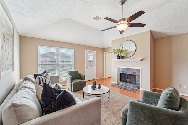 living area featuring visible vents, a tiled fireplace, vaulted ceiling, wood finished floors, and a ceiling fan