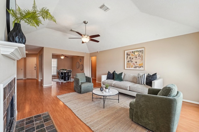 living room featuring visible vents, a fireplace with flush hearth, dark wood finished floors, and a ceiling fan