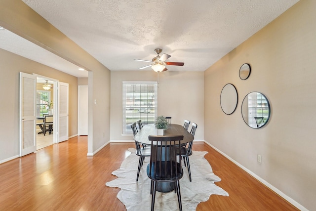 dining area featuring a ceiling fan, baseboards, light wood finished floors, and a textured ceiling