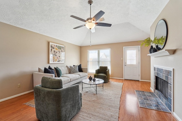 living room with a ceiling fan, lofted ceiling, wood finished floors, and a tile fireplace