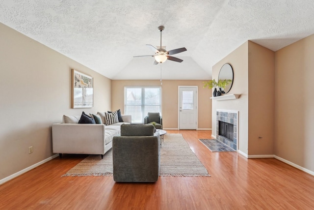 living room featuring wood finished floors, baseboards, lofted ceiling, a fireplace, and ceiling fan