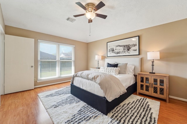 bedroom featuring a textured ceiling, wood finished floors, visible vents, and baseboards