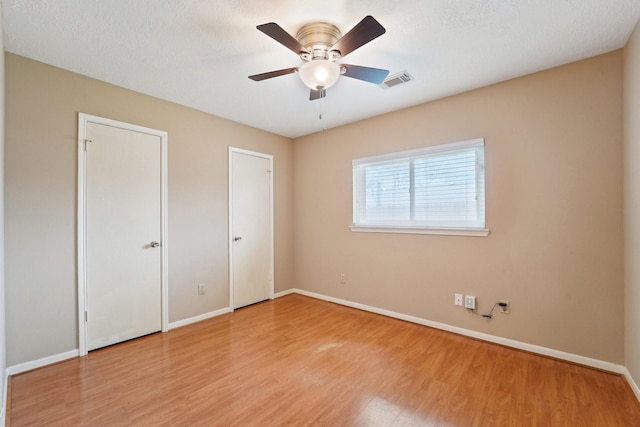 unfurnished bedroom featuring visible vents, light wood-style flooring, baseboards, and multiple closets