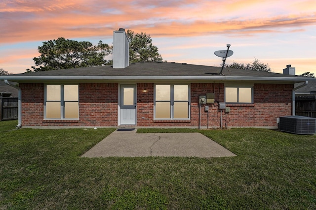 back of property at dusk with central AC unit, a lawn, a chimney, and fence