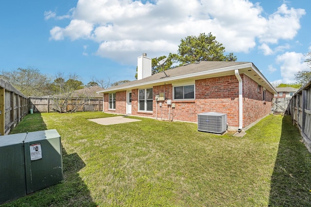 back of property featuring brick siding, central AC unit, a lawn, and a fenced backyard